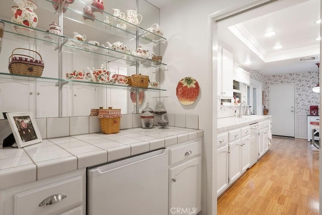 bar featuring crown molding, a sink, light wood finished floors, a raised ceiling, and wallpapered walls