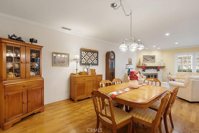 dining space featuring crown molding, recessed lighting, visible vents, light wood-style floors, and a glass covered fireplace