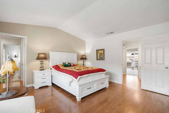 bedroom featuring lofted ceiling, visible vents, baseboards, and wood finished floors