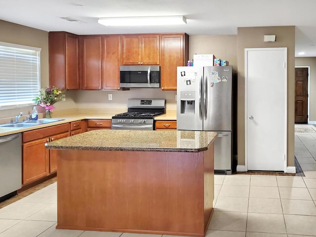 kitchen with light stone counters, a kitchen island, light tile patterned floors, and appliances with stainless steel finishes