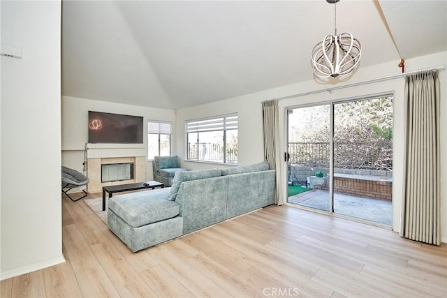 living room with vaulted ceiling, light hardwood / wood-style flooring, a notable chandelier, and a tiled fireplace