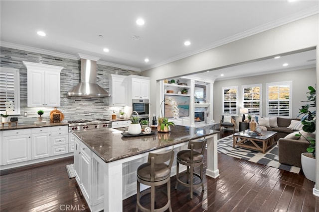 kitchen with appliances with stainless steel finishes, dark wood-type flooring, wall chimney range hood, white cabinetry, and a large island