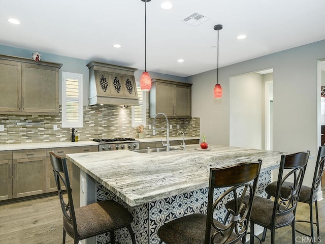 kitchen with light wood-type flooring, premium range hood, sink, hanging light fixtures, and a breakfast bar area