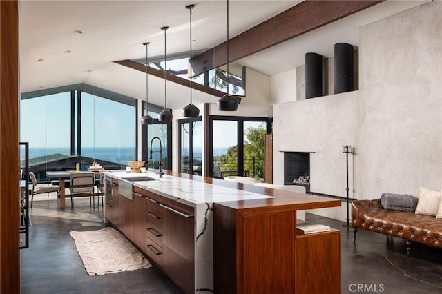 kitchen with sink, lofted ceiling with beams, decorative light fixtures, a water view, and a large island