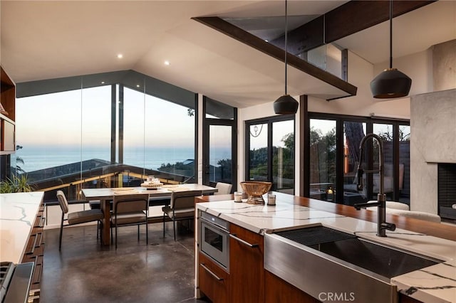 kitchen featuring sink, decorative light fixtures, a water view, a fireplace, and lofted ceiling