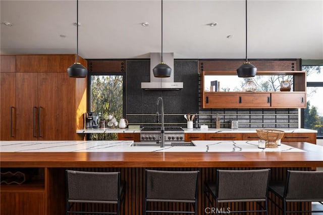 kitchen featuring tasteful backsplash, wall chimney exhaust hood, hanging light fixtures, and a breakfast bar area