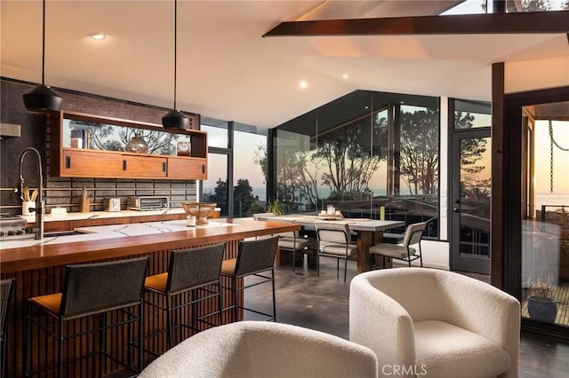 bar featuring hanging light fixtures, backsplash, a wealth of natural light, and vaulted ceiling