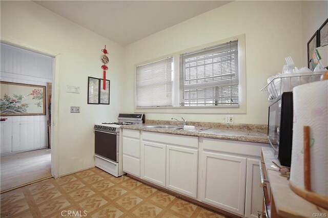 kitchen with white range oven, white cabinetry, and sink