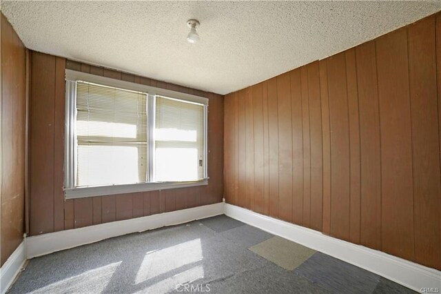 carpeted spare room with wood walls and a textured ceiling