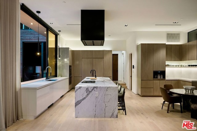 kitchen with sink, light wood-type flooring, a kitchen island with sink, and a kitchen breakfast bar