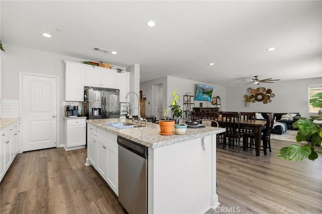 kitchen with sink, appliances with stainless steel finishes, white cabinetry, wood-type flooring, and an island with sink