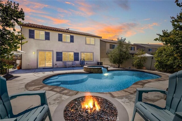 pool at dusk with a patio area, an in ground hot tub, and a fire pit