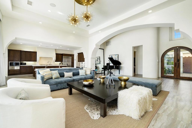 living room featuring a raised ceiling, french doors, a towering ceiling, and a chandelier