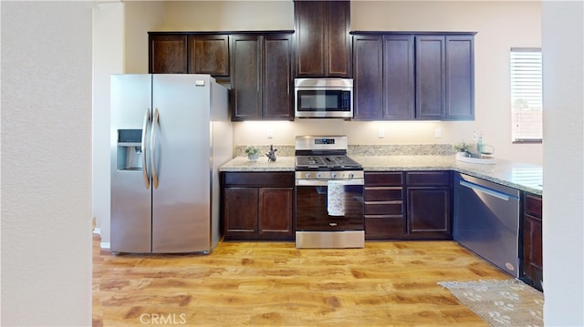 kitchen featuring dark brown cabinets, light stone counters, stainless steel appliances, and light hardwood / wood-style floors