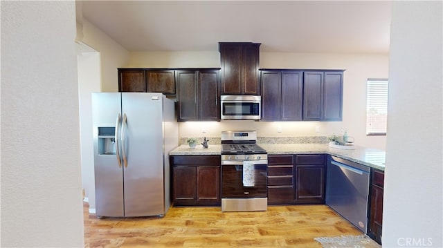 kitchen featuring light wood-type flooring, appliances with stainless steel finishes, dark brown cabinets, and light stone countertops