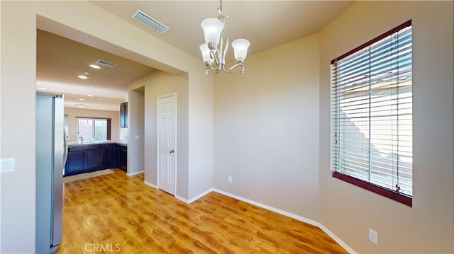 unfurnished dining area with light hardwood / wood-style floors and an inviting chandelier