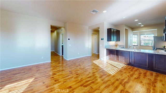 kitchen with light hardwood / wood-style floors, sink, stainless steel fridge, dark brown cabinets, and light stone counters