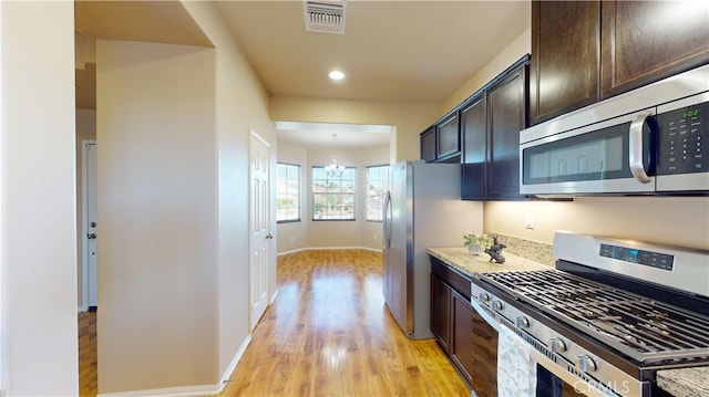 kitchen with appliances with stainless steel finishes, light stone counters, a chandelier, and dark brown cabinetry