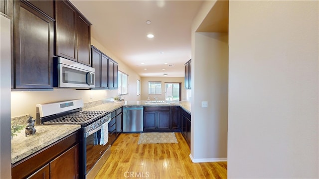 kitchen with kitchen peninsula, light wood-type flooring, light stone countertops, stainless steel appliances, and dark brown cabinets