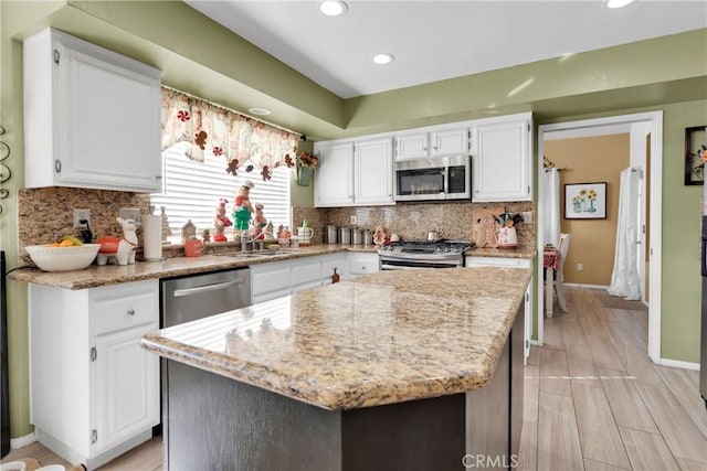 kitchen with white cabinets, appliances with stainless steel finishes, a kitchen island, and light stone countertops