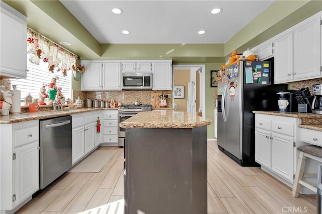 kitchen with light stone countertops, stainless steel appliances, light hardwood / wood-style flooring, white cabinets, and a kitchen island