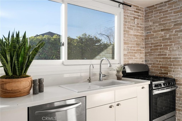 kitchen featuring sink, white cabinetry, stainless steel appliances, and brick wall