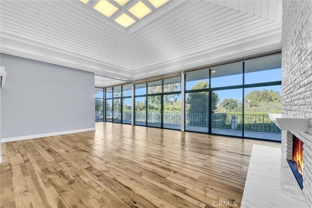 unfurnished living room with a wall of windows, a fireplace, a towering ceiling, and light hardwood / wood-style flooring