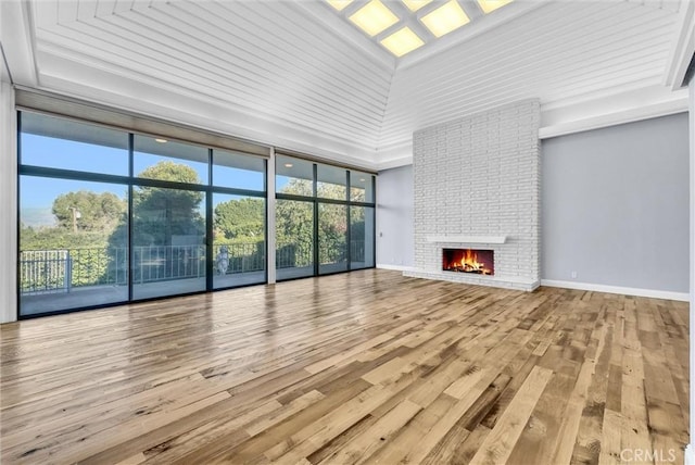 unfurnished living room with a brick fireplace, a wall of windows, a high ceiling, and light wood-type flooring