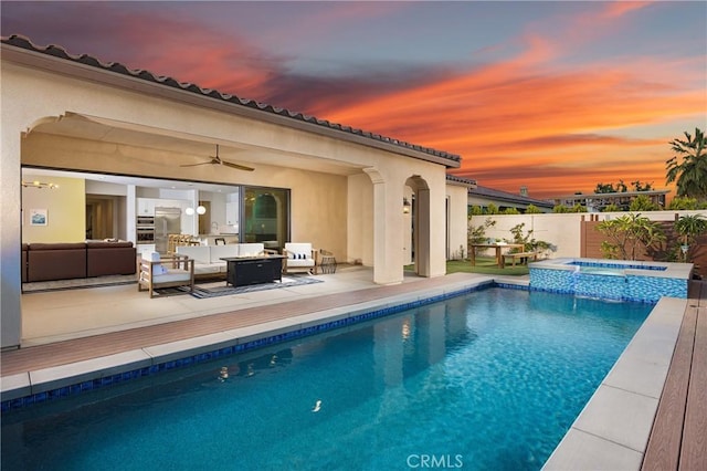 pool at dusk with a pool with connected hot tub, a fenced backyard, and an outdoor living space