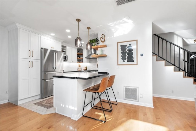 kitchen with white cabinets, a kitchen bar, appliances with stainless steel finishes, and light hardwood / wood-style flooring