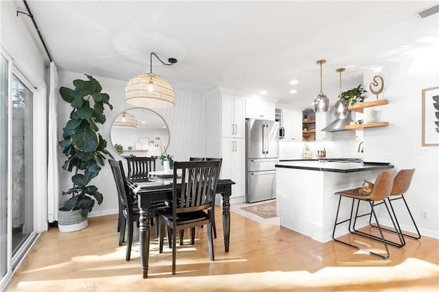 kitchen featuring kitchen peninsula, light wood-type flooring, high quality fridge, decorative light fixtures, and white cabinets