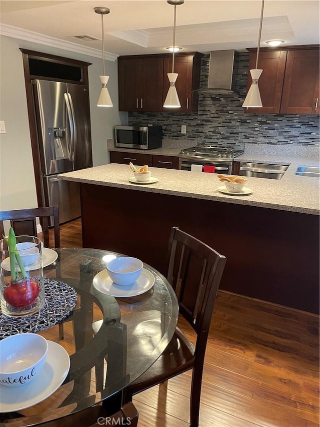 kitchen featuring light wood-type flooring, ornamental molding, wall chimney exhaust hood, stainless steel appliances, and hanging light fixtures