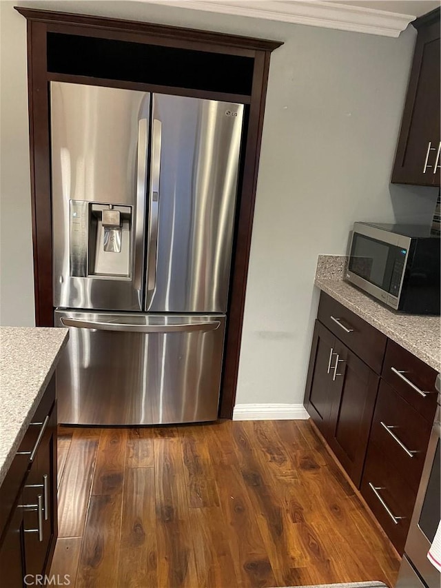 kitchen with dark wood-type flooring, crown molding, appliances with stainless steel finishes, light stone counters, and dark brown cabinetry