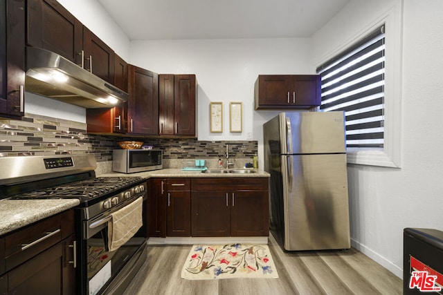 kitchen with light stone countertops, sink, stainless steel appliances, backsplash, and light hardwood / wood-style floors