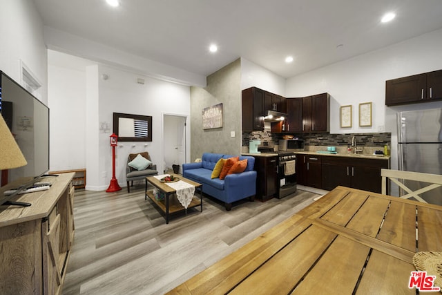 kitchen with backsplash, dark brown cabinetry, stainless steel appliances, sink, and light hardwood / wood-style floors