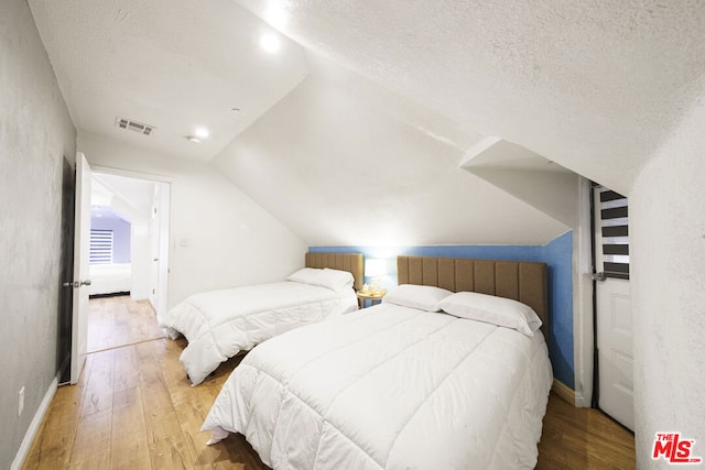 bedroom with light wood-type flooring, a textured ceiling, radiator, and vaulted ceiling