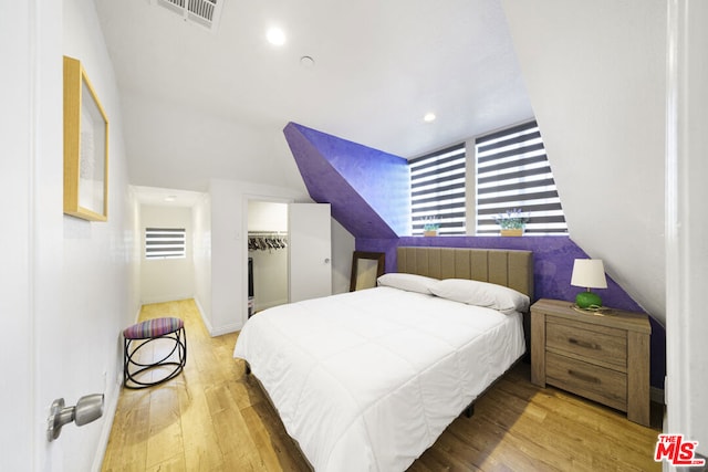 bedroom featuring radiator heating unit, vaulted ceiling, a walk in closet, a closet, and hardwood / wood-style flooring