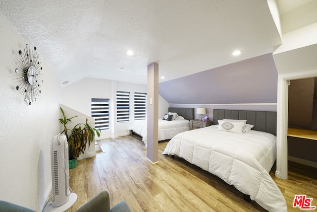 bedroom with a textured ceiling, light hardwood / wood-style floors, and lofted ceiling