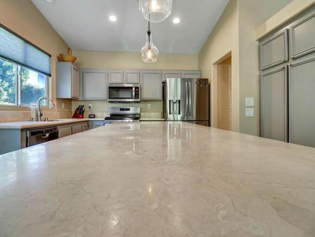 kitchen with gray cabinetry, decorative light fixtures, light stone countertops, and appliances with stainless steel finishes