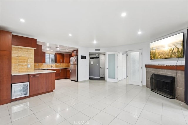 kitchen with backsplash, light tile patterned floors, a fireplace, and stainless steel refrigerator