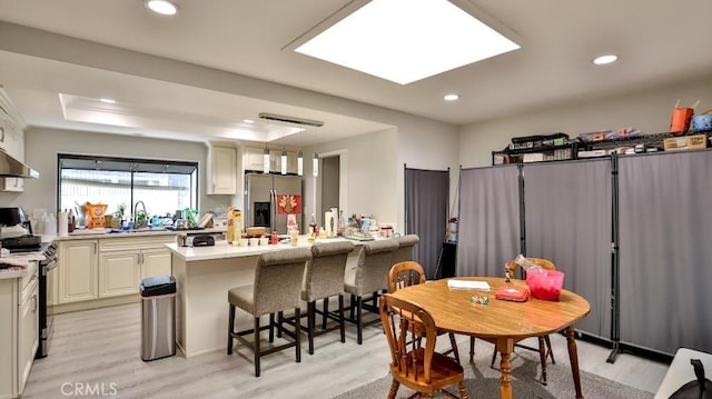 kitchen featuring a kitchen bar, stainless steel appliances, sink, light hardwood / wood-style floors, and hanging light fixtures