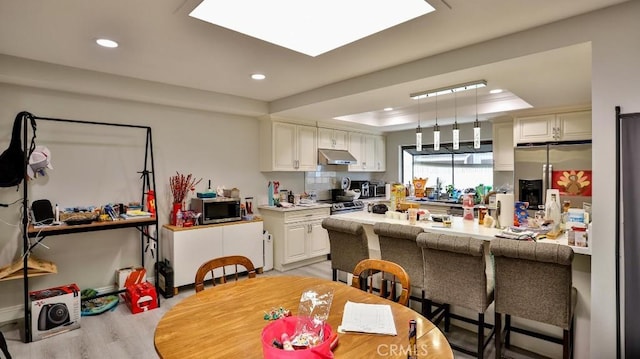 kitchen featuring kitchen peninsula, appliances with stainless steel finishes, a raised ceiling, light hardwood / wood-style flooring, and white cabinetry