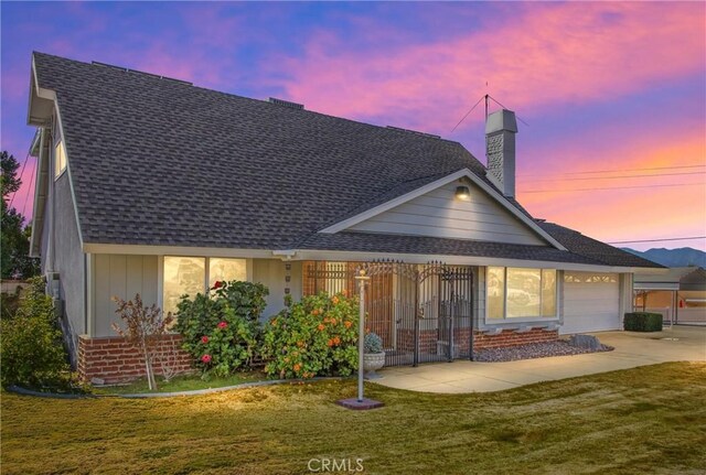 back house at dusk with a lawn and a garage