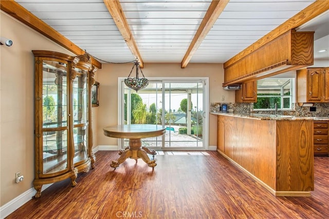 kitchen with beamed ceiling, decorative backsplash, light stone countertops, and dark wood-type flooring