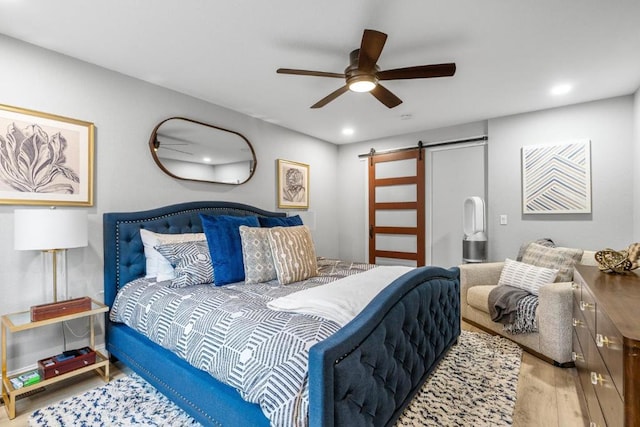 bedroom featuring hardwood / wood-style floors, ceiling fan, and a barn door