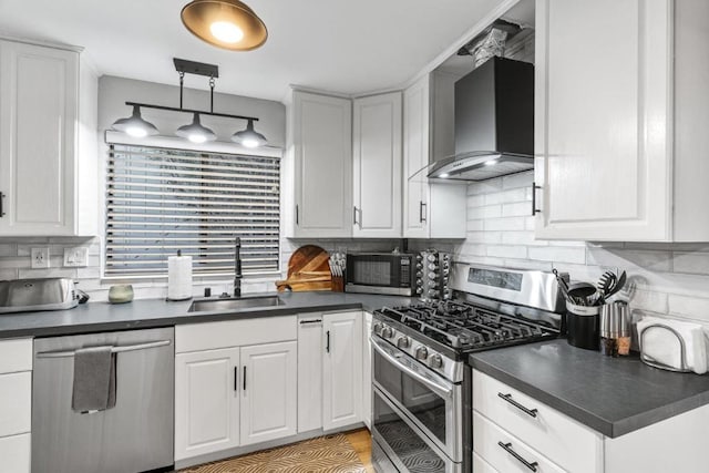 kitchen featuring appliances with stainless steel finishes, wall chimney exhaust hood, sink, decorative light fixtures, and white cabinets