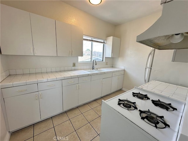 kitchen featuring exhaust hood, white cabinets, tile counters, sink, and white gas stove