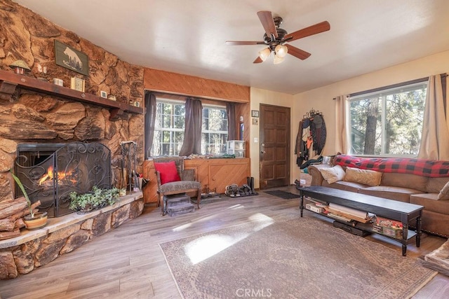 living room featuring light wood-type flooring, a stone fireplace, ceiling fan, and a healthy amount of sunlight