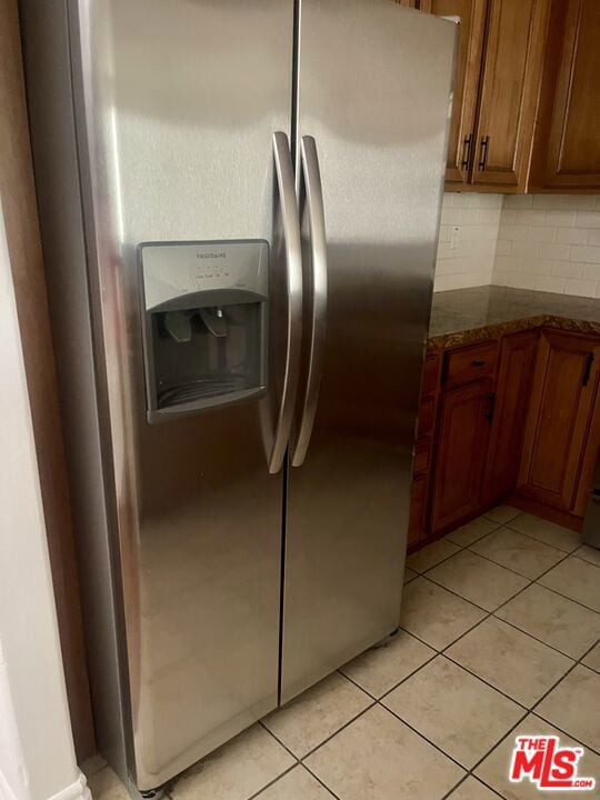 kitchen with stainless steel fridge with ice dispenser, backsplash, light tile patterned floors, and dark stone counters