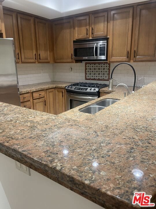 kitchen with decorative backsplash, sink, stainless steel appliances, and dark stone counters